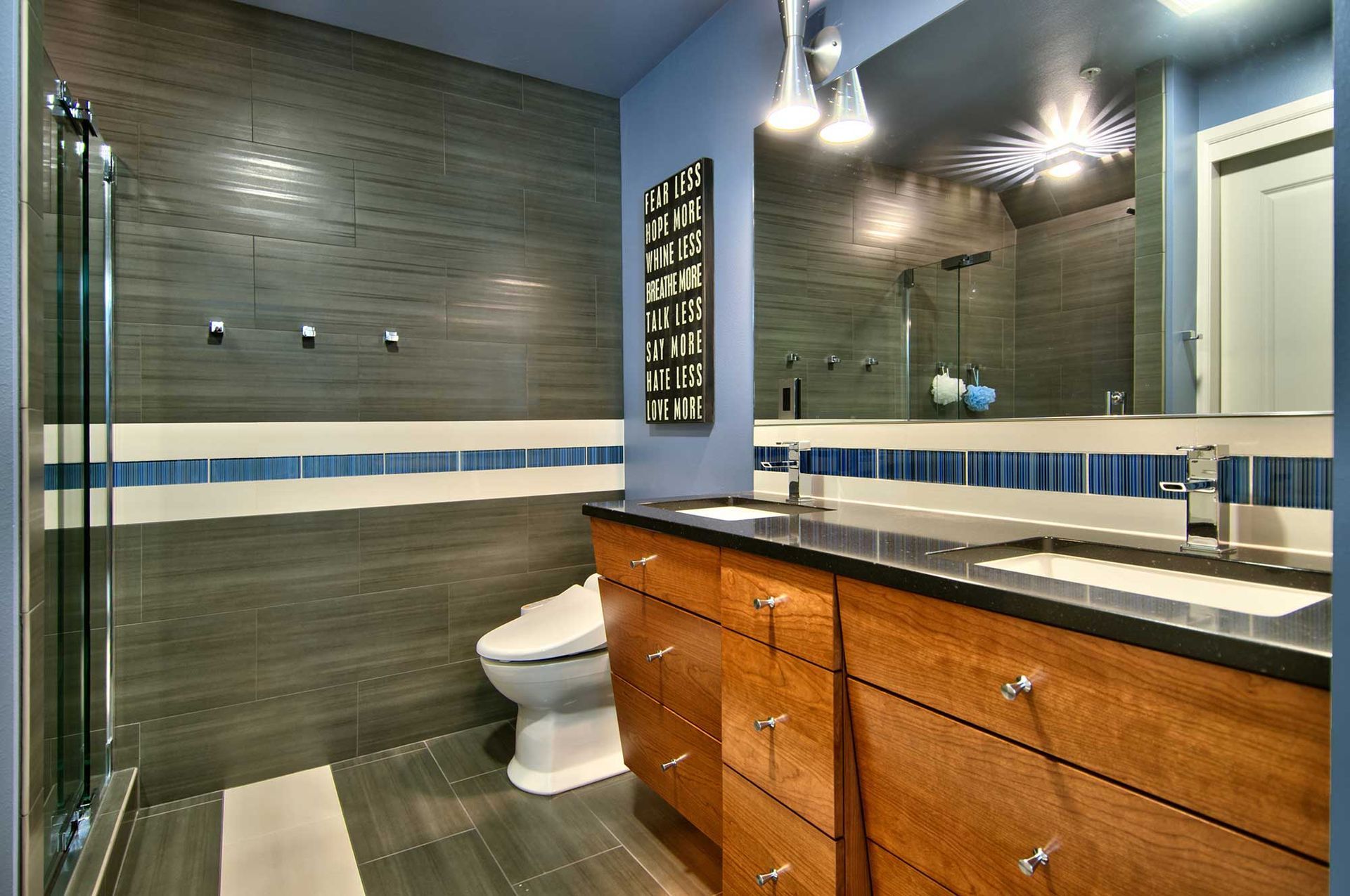Modern bathroom with gray tiled walls, a wooden vanity, and blue accents.