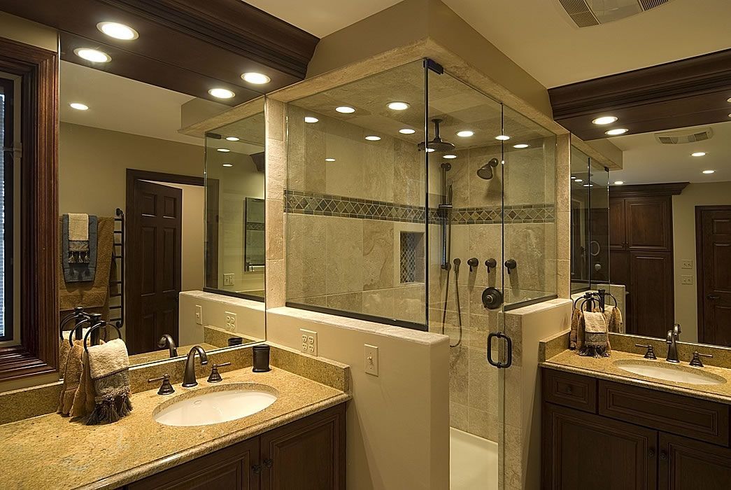 Bathroom with a glass shower, two sinks, and wood cabinetry. Gold countertops and beige tiling.