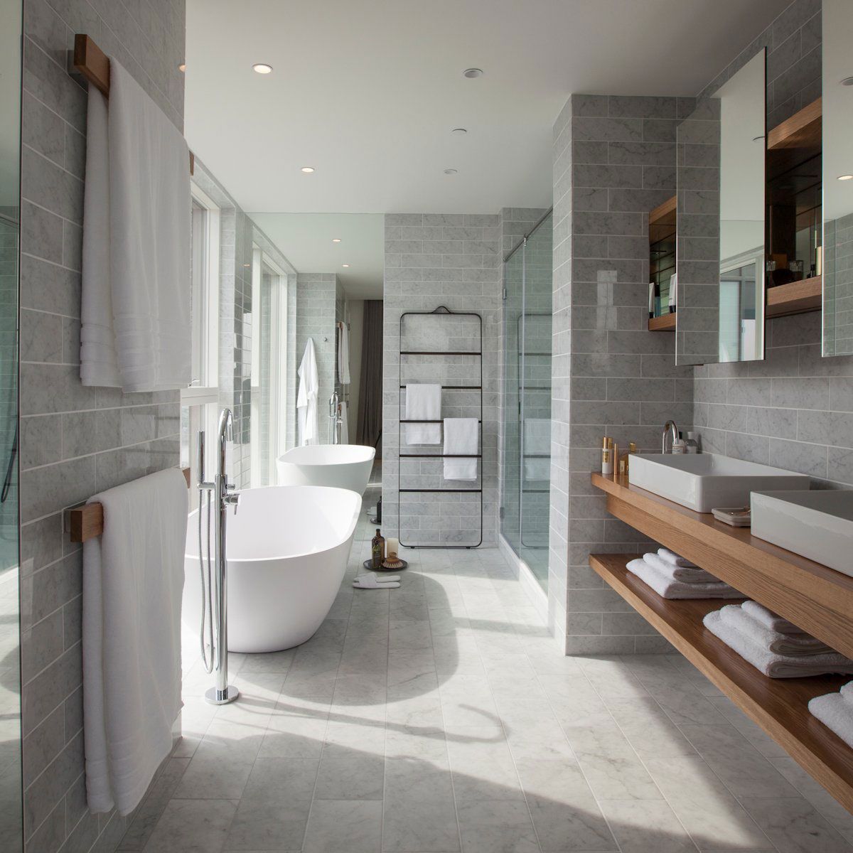 Modern bathroom with a freestanding tub, dual sinks, and gray tile walls.