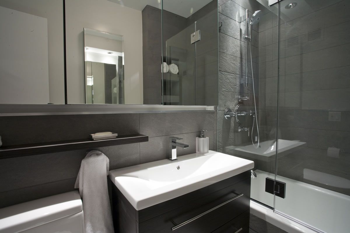 Modern bathroom with gray tiles, shower, vanity, and mirror. White sink and towel.