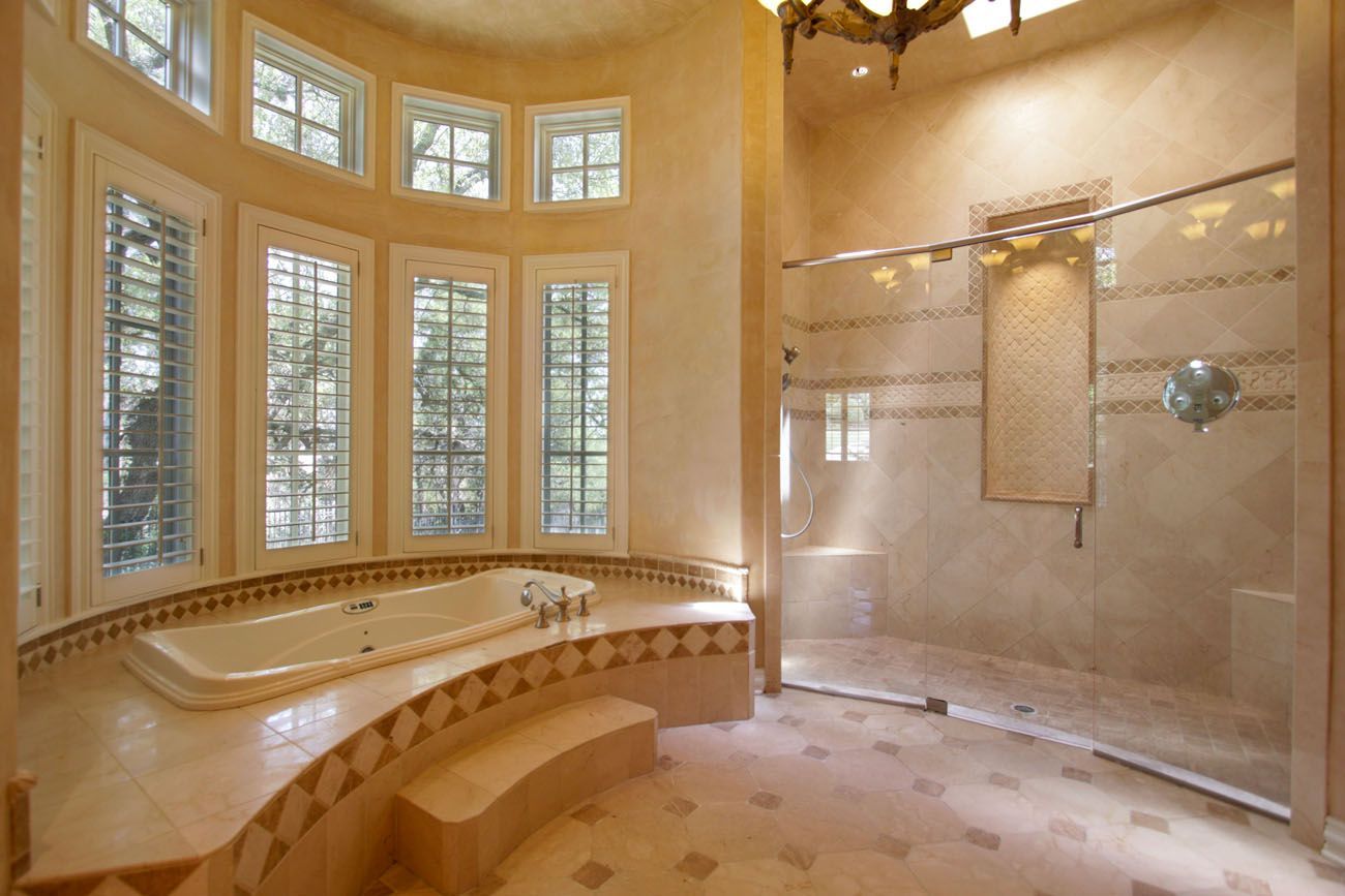 Luxury bathroom with curved windows, a built-in tub, and a glass shower, all in shades of beige.