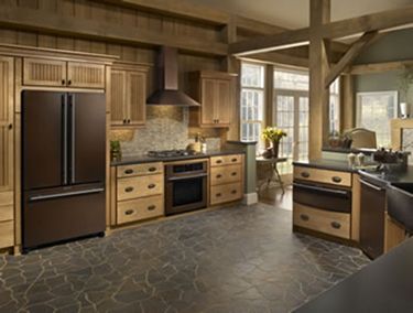 Brown and tan rustic kitchen with refrigerator, cabinets, and stove. Stone floor.