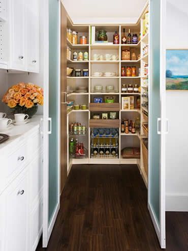 Walk-in pantry with white shelves filled with food items, framed by white doors and dark wood floor.