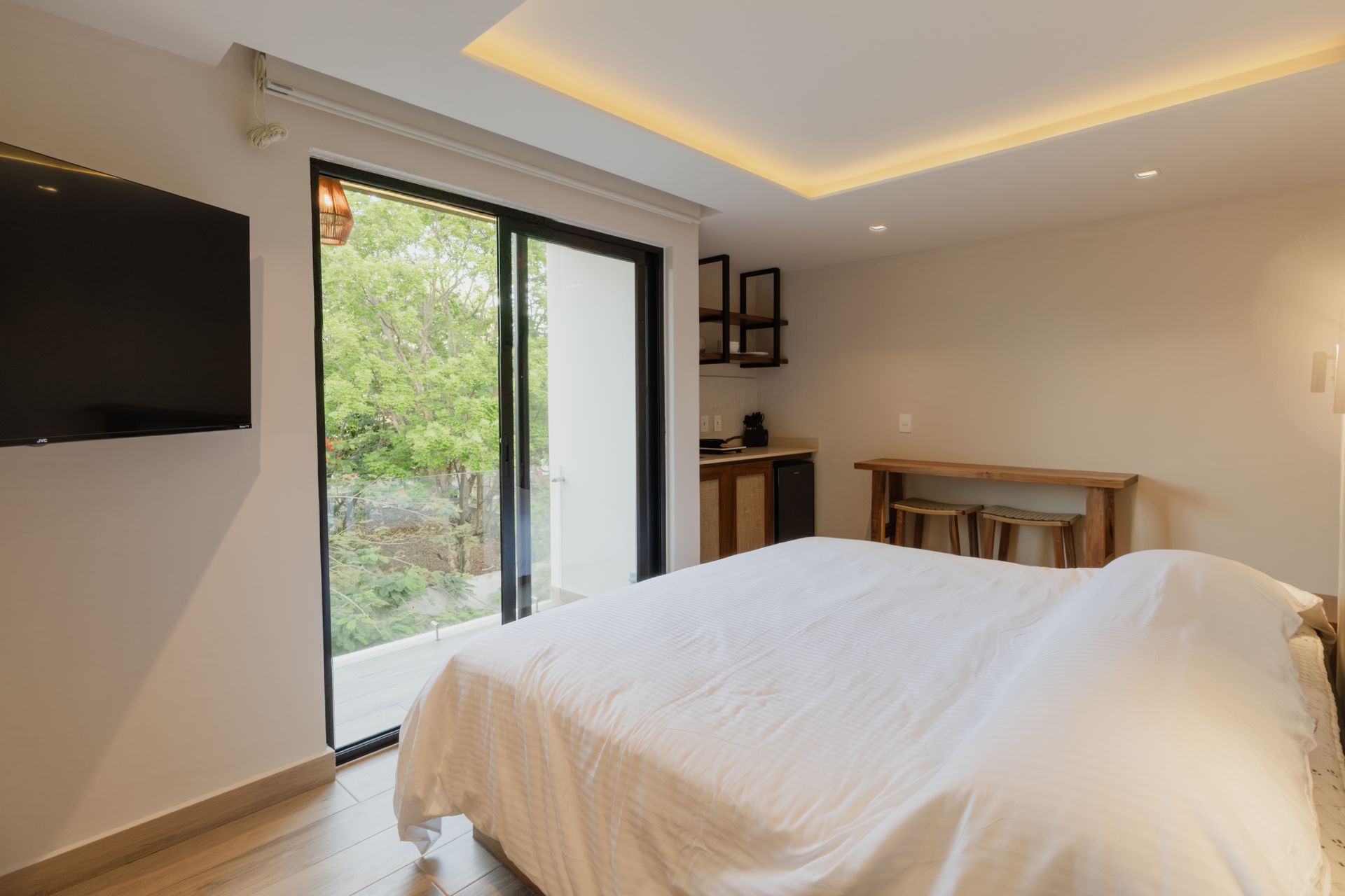 Habitación luminosa y moderna con cama, escritorio, armario con espejo y grandes cortinas.