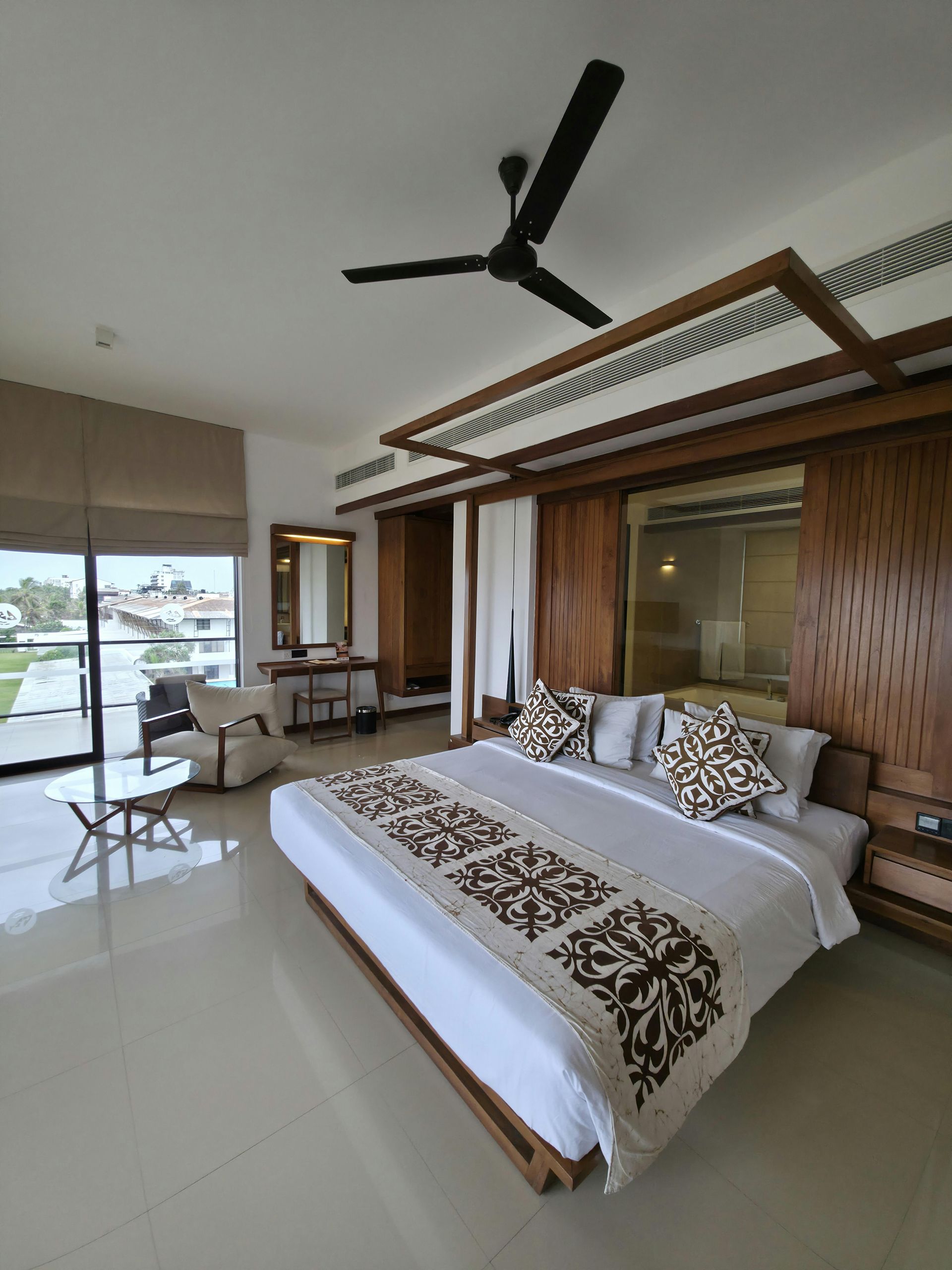 Dormitorio moderno con cama con dosel, ventilador de techo y puertas correderas que dan a un balcón con vistas.