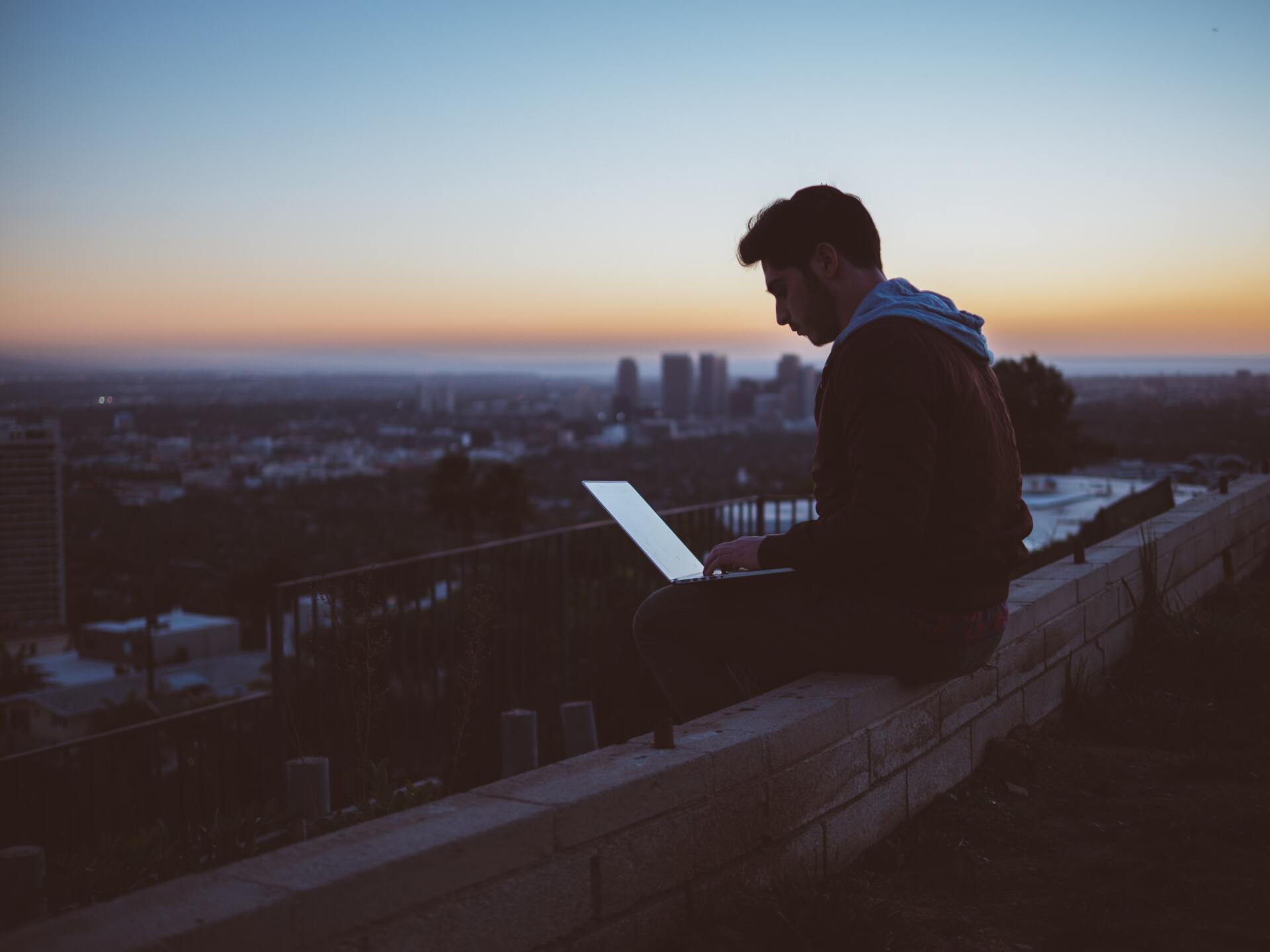 Silhouette of man on ledge using computer thinking of getting a website in the sunset