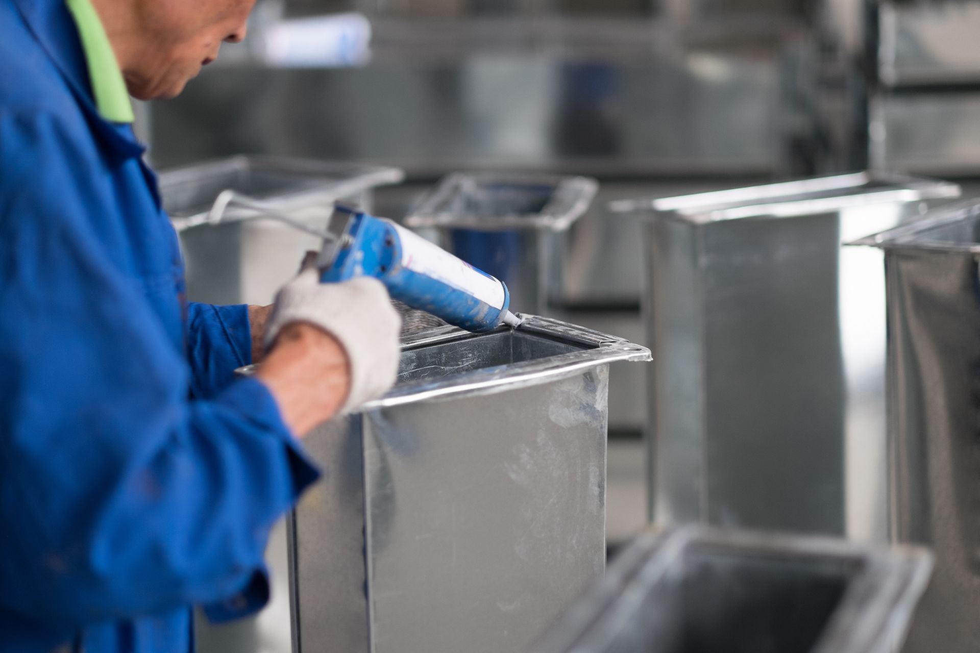 A man is applying glue to a metal duct in a factory.