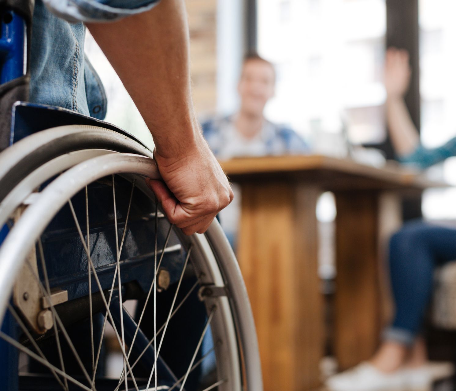 An individual in a wheelchair coming towards two others sitting at a table