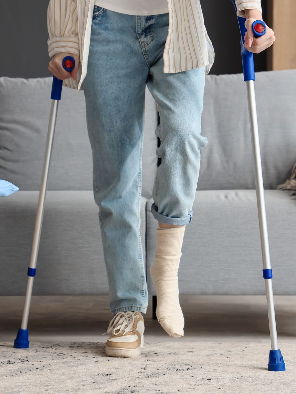A person wearing jeans and walking with a pair of crutches