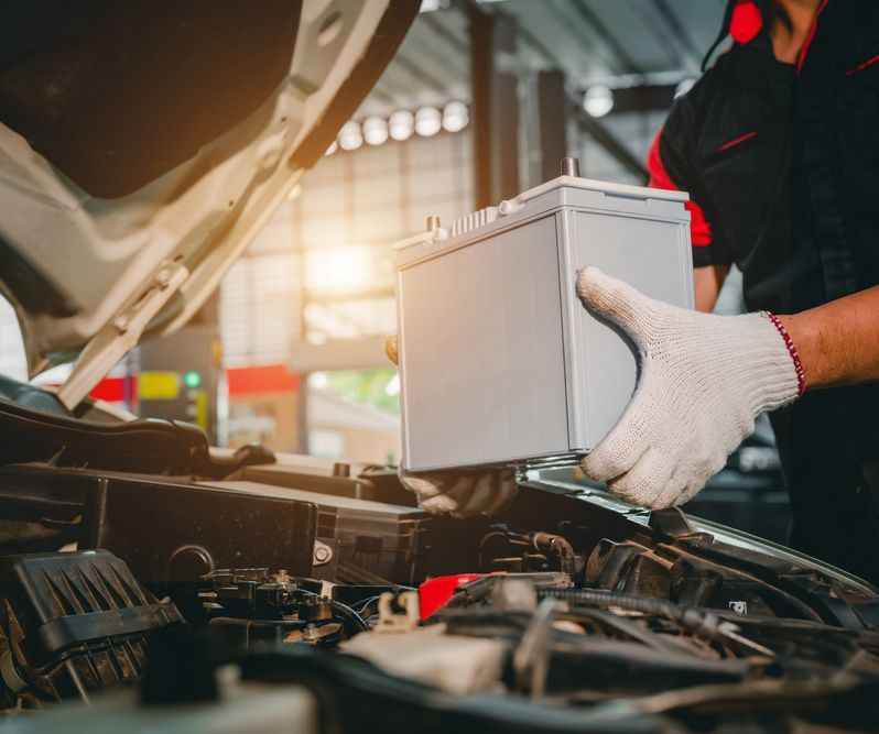 Car-mechanic in a service center picking up a new battery — A Grade Oils & Batteries In Wodonga VIC