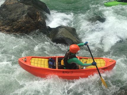 A person in an orange kayak is paddling through a river