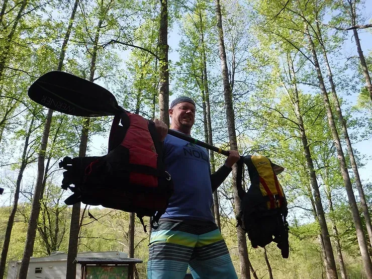 a man is holding a paddle and a backpack in the woods 