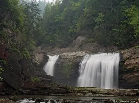 A waterfall is surrounded by trees and rocks in the middle of a forest.