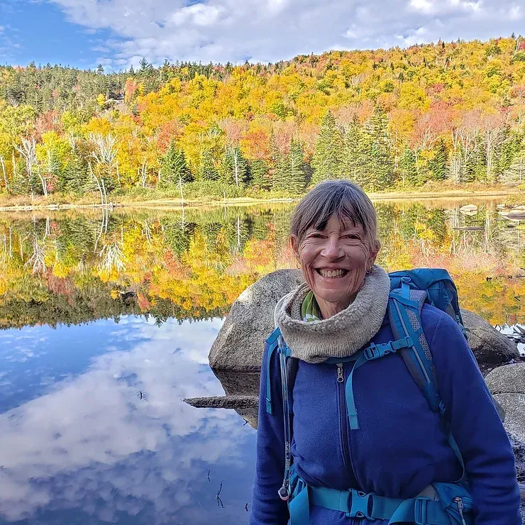 A woman with a backpack is standing next to a lake.