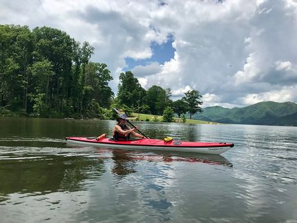 A person is riding a red kayak on a lake.