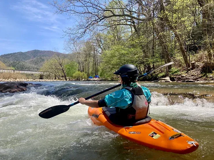 A man is paddling an orange kayak down a river.