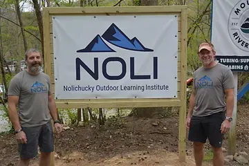 Two men are standing in front of a noli outdoor learning institute sign.