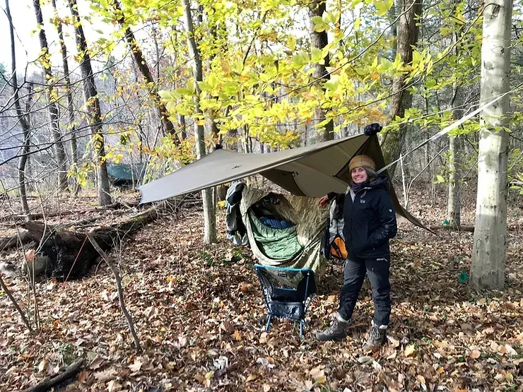 A person is standing next to a hammock in the woods.