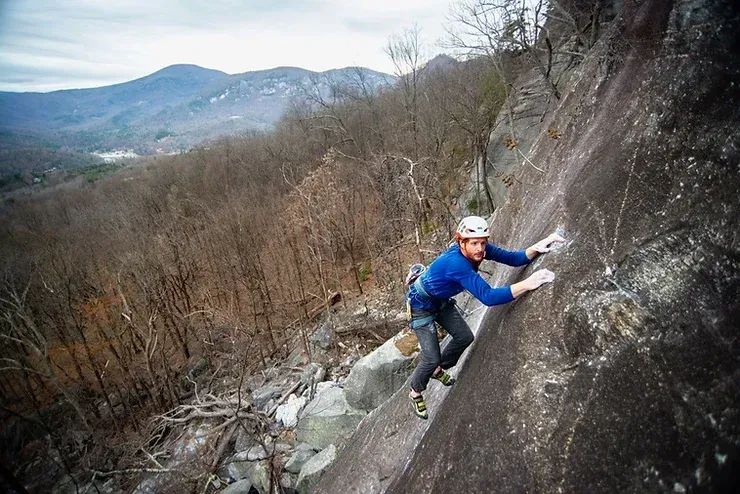 A man is climbing up a rock wall in the woods.