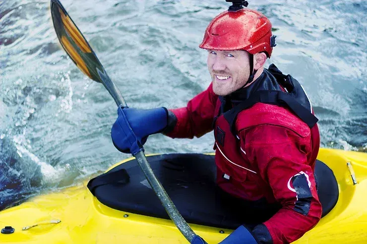 A man in a red jacket is paddling a yellow kayak.