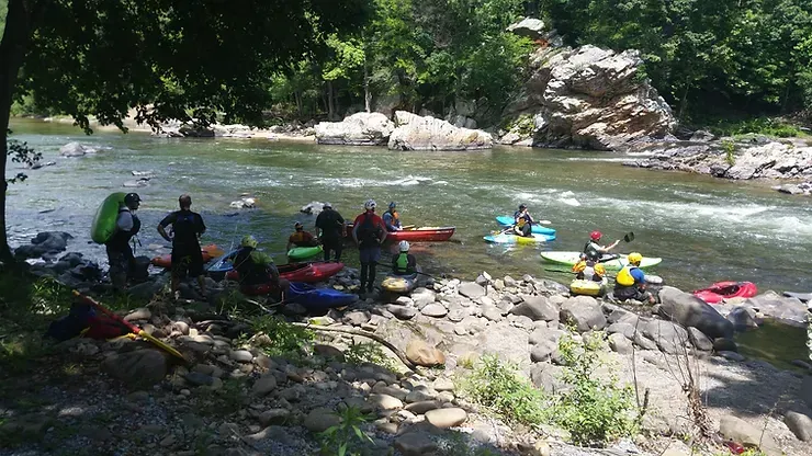 A group of people in kayaks are standing on the shore of a river.