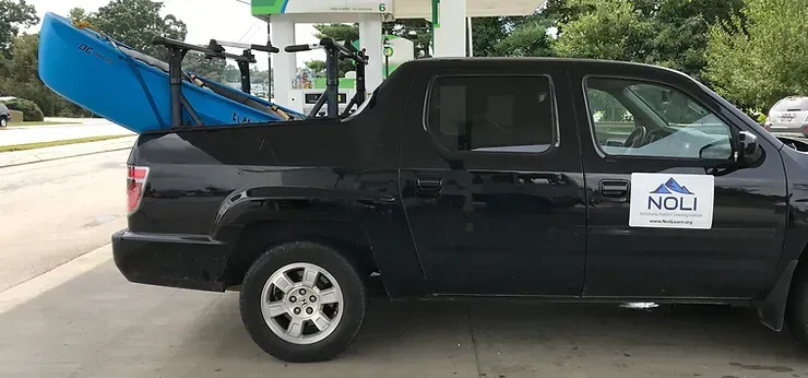 A black truck with a blue kayak in the bed is parked at a gas station.