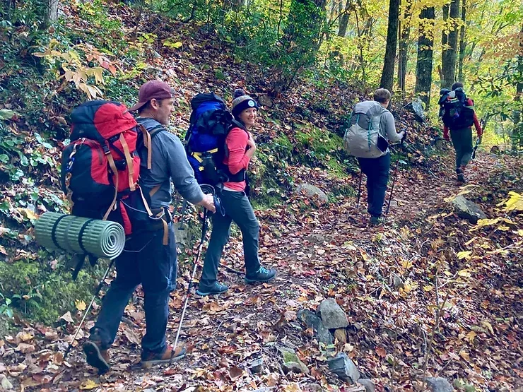 A group of people with backpacks are walking down a path in the woods.