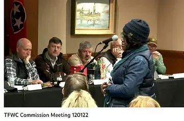 A woman is speaking into a microphone while sitting at a table with other people.