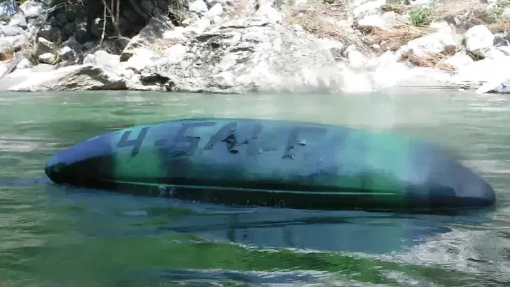 A green and black kayak is floating on top of a river.