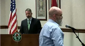 A man with a beard is standing at a podium talking into a microphone.