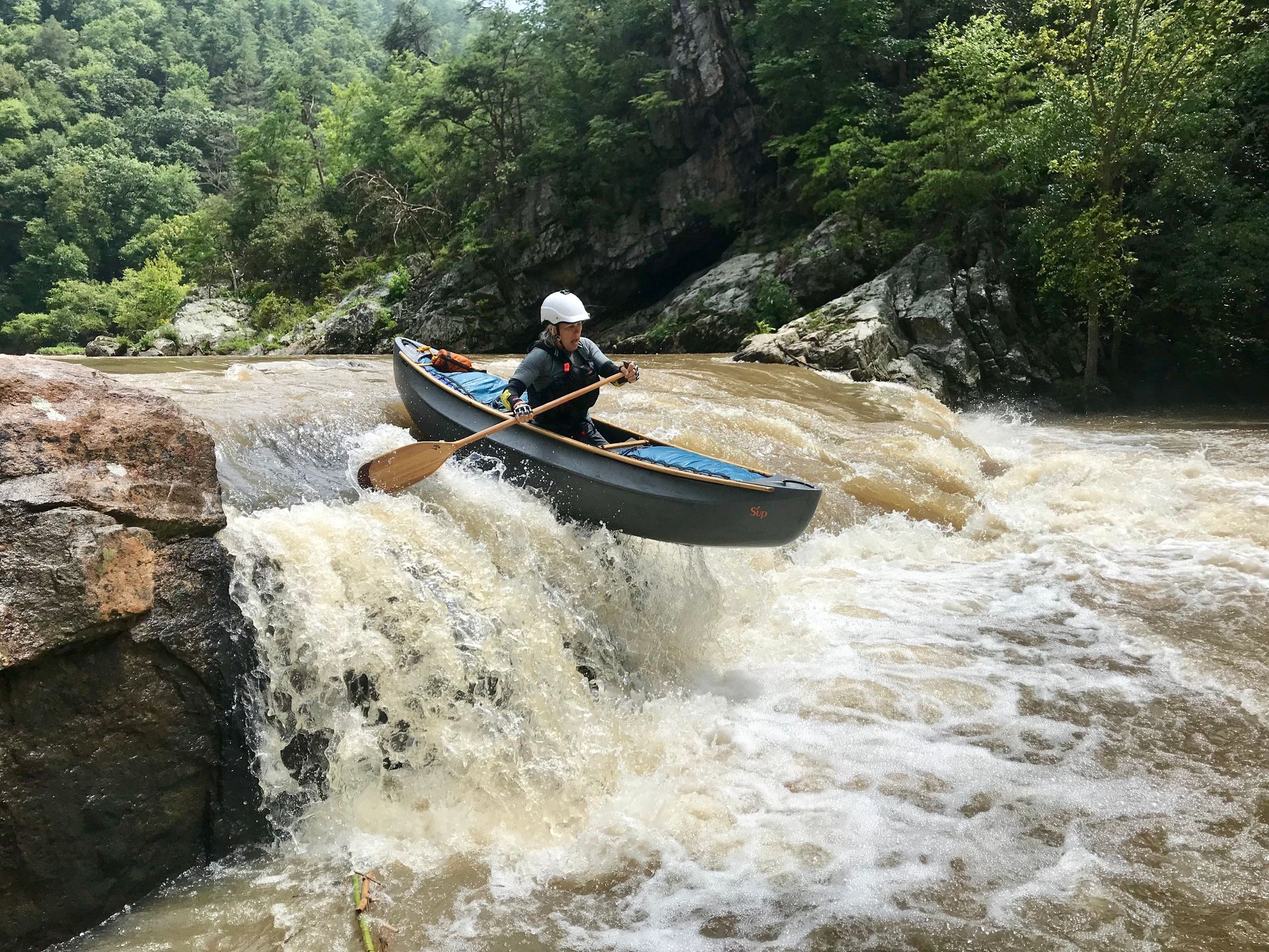Person in canoe navigating small waterfall in river.
