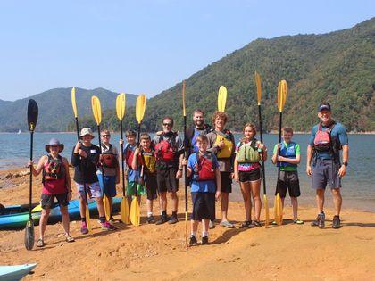 A group of people standing on a beach holding kayak paddles.