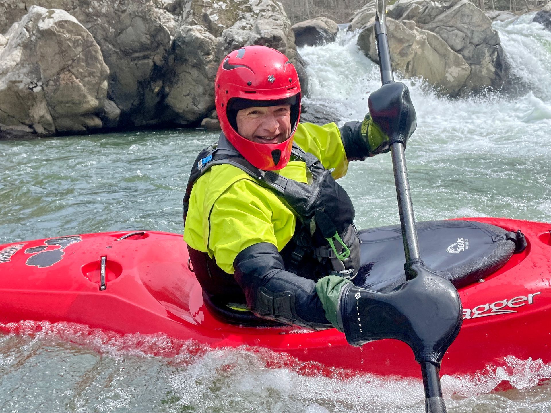 A man in a red kayak is paddling down a river.