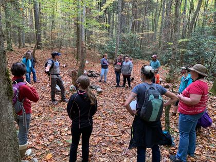 A group of people are standing in a circle in the woods.