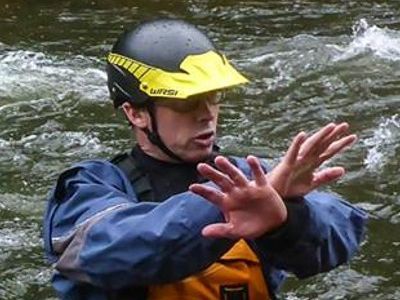 A man wearing a helmet and a life jacket is standing in the water.