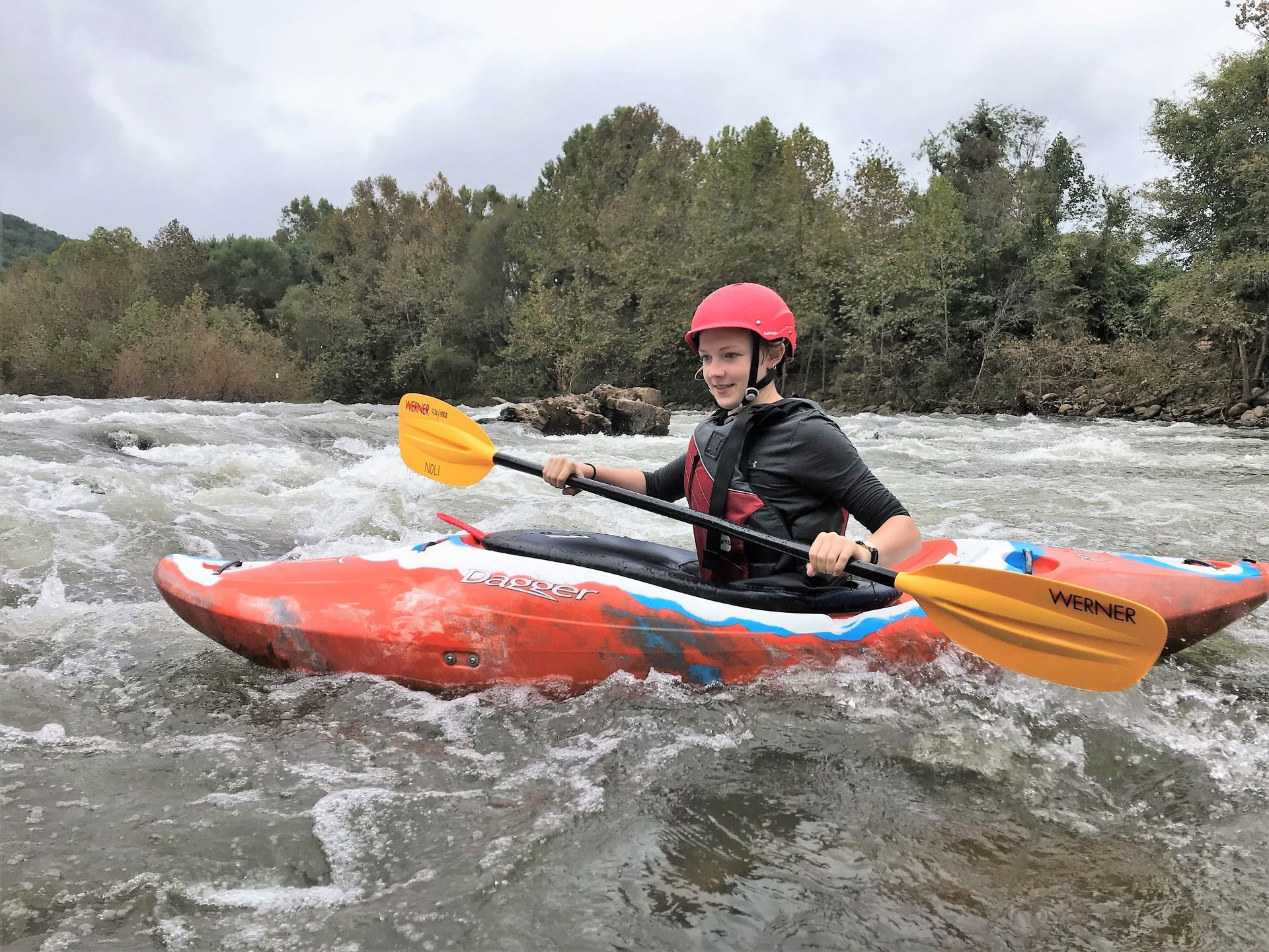 A man in a red helmet is riding a kayak down a river.