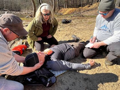 A group of people are kneeling around a person laying on the ground.