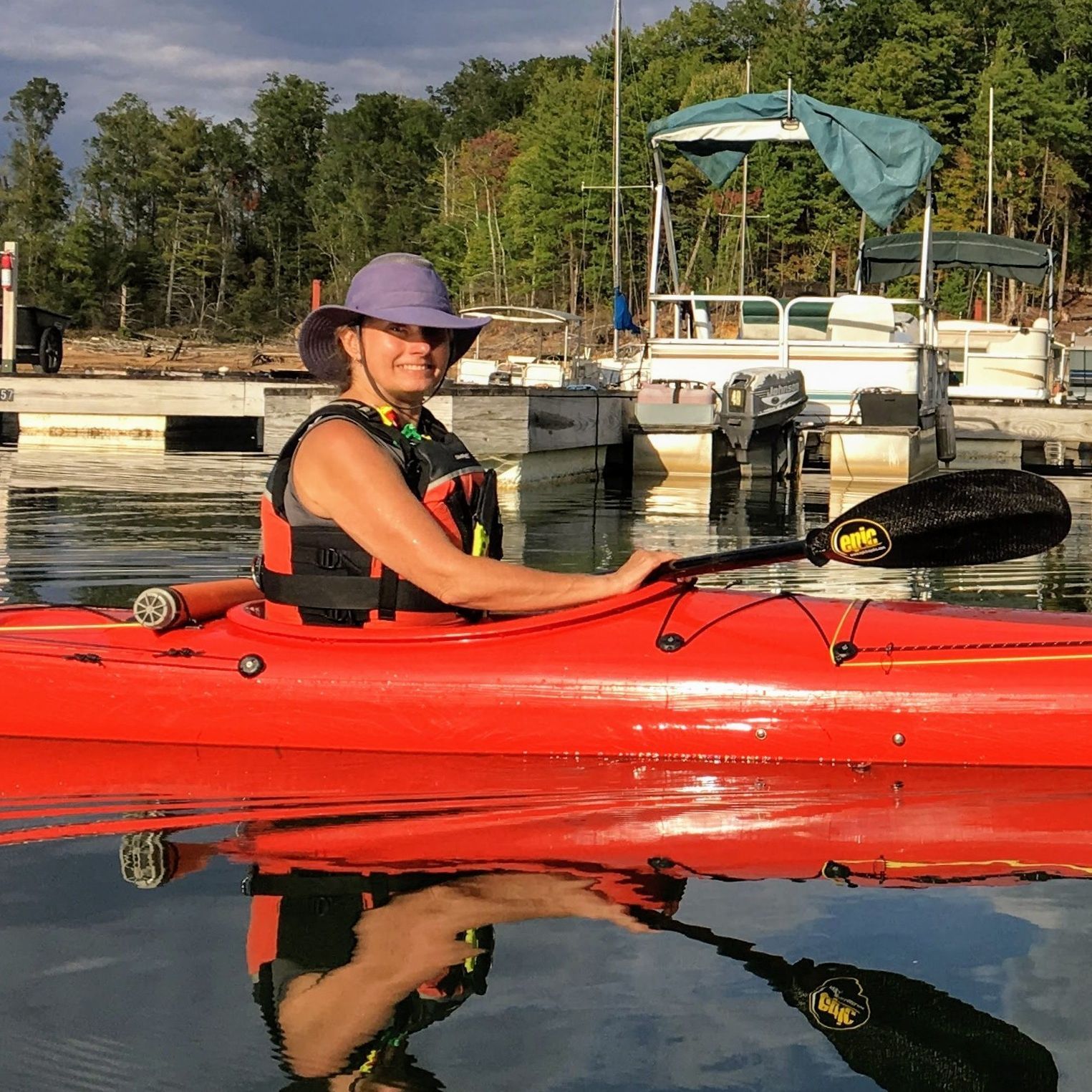 A woman in a purple hat is sitting in a red kayak