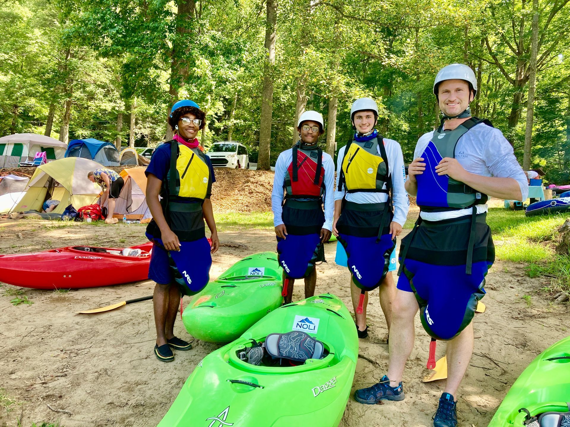 A group of people are standing next to kayaks on the beach.