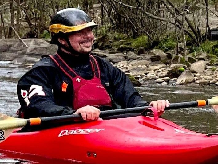 A man is rowing a red kayak in a river.