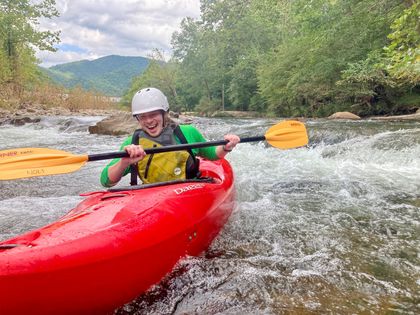 A person is paddling a red kayak down a river.