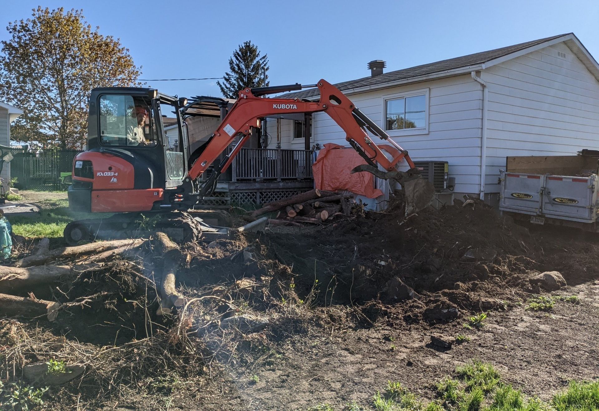 Une excavatrice creuse un trou devant une maison