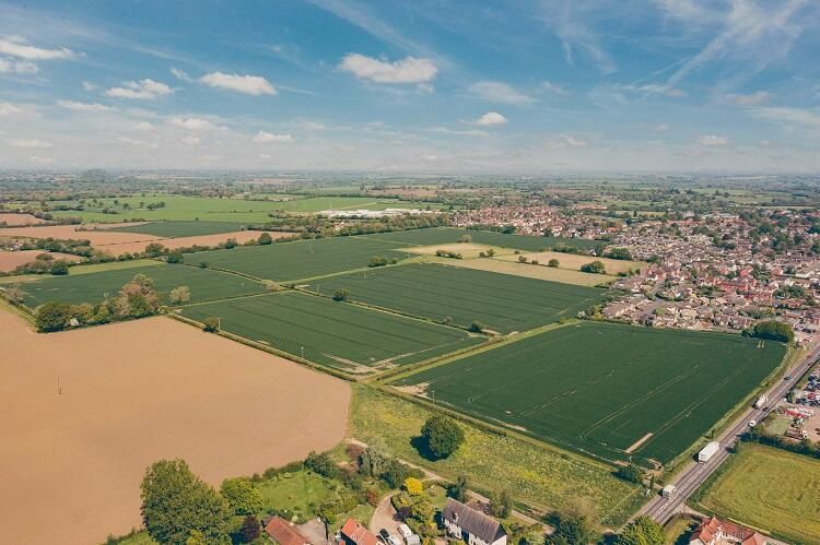 Aerial view of green fields and a brown flooded area next to a town under a blue sky.