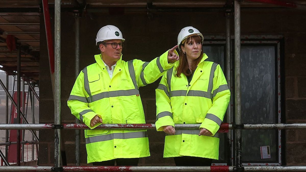 Two people in hard hats and high-vis vests on a construction site, one pointing, both looking outward.