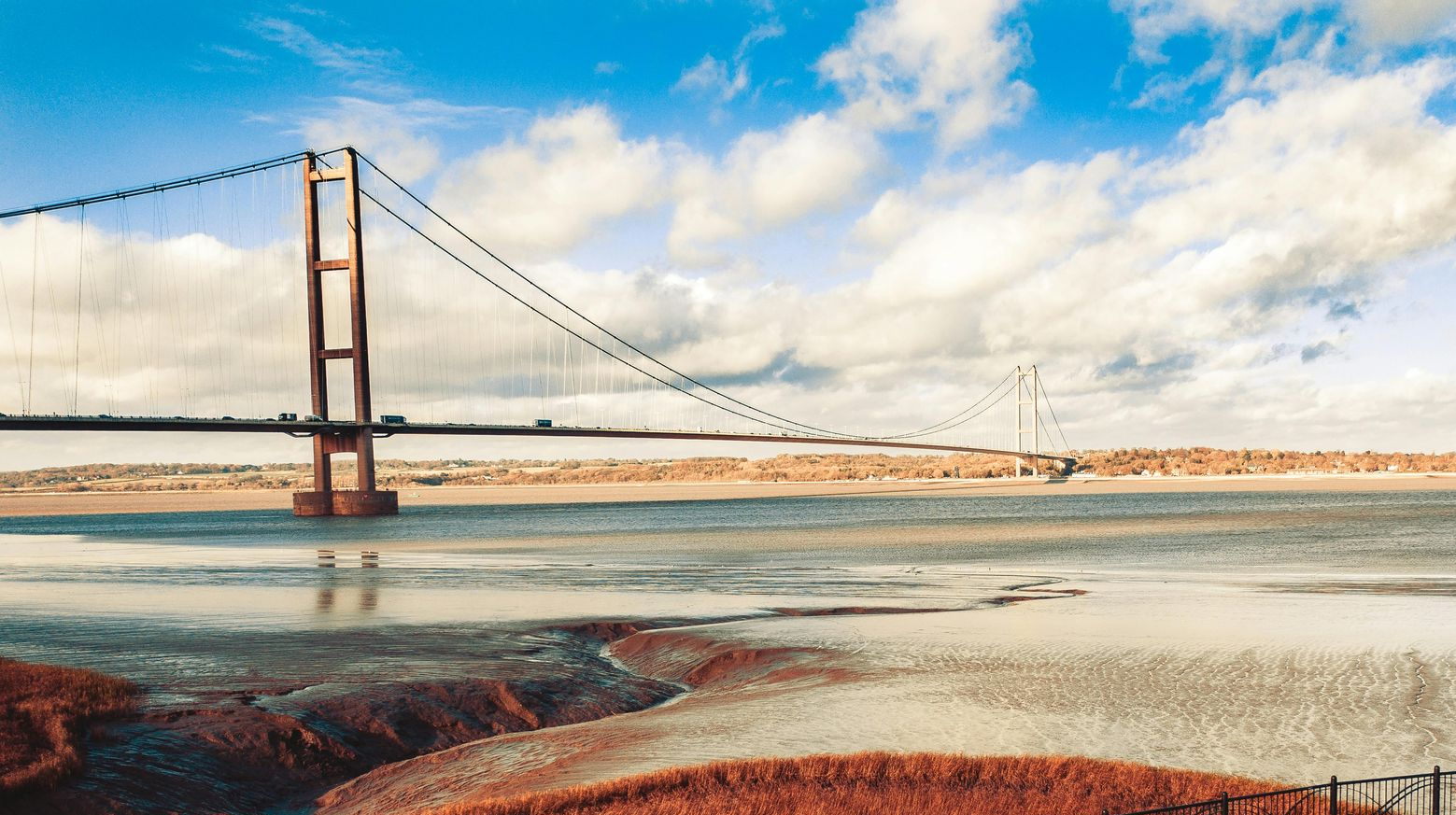 Golden Gate Bridge over a body of water, cloudy blue sky.