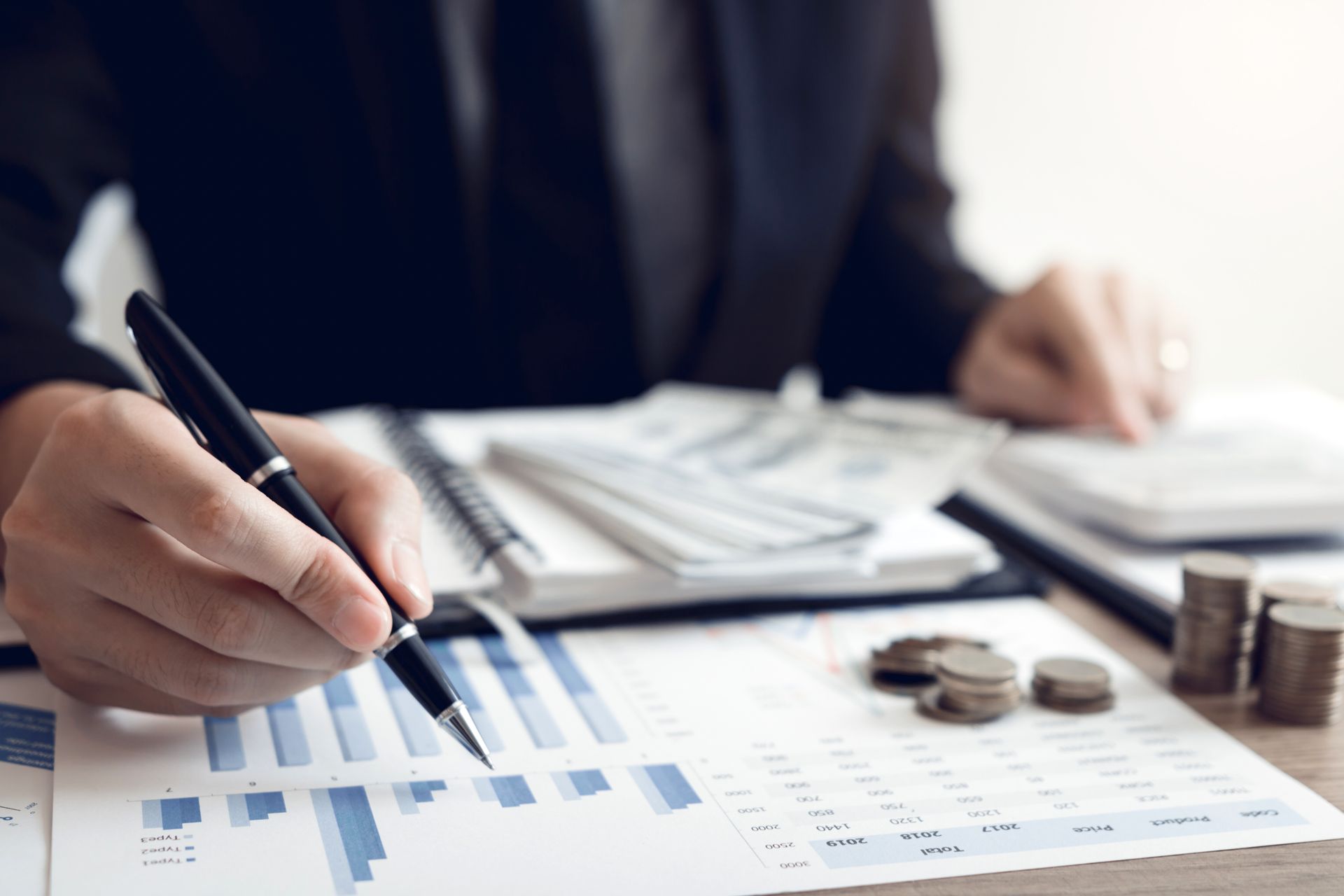 A man looking at documents on the table with money on the documents and a pen in his hand.