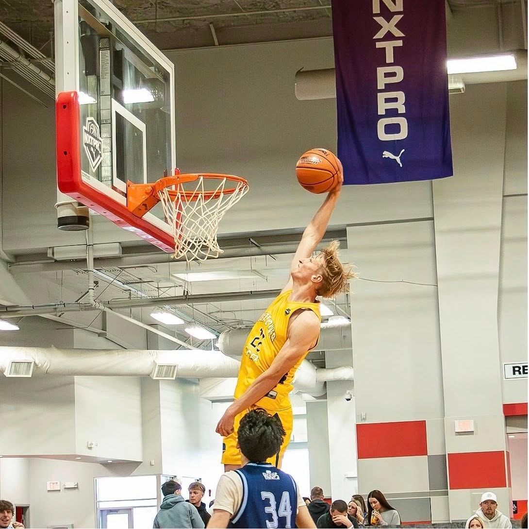 Basketball player in yellow jersey leaping for a layup over a defender near the hoop
