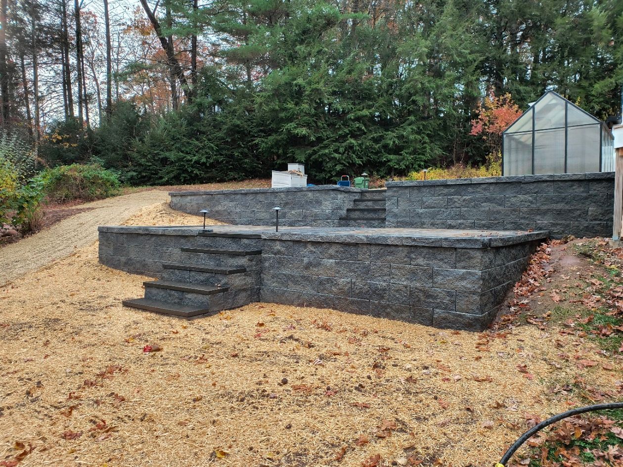 Stone retaining walls with steps in a yard covered in small brown stones. Greenhouse in background.