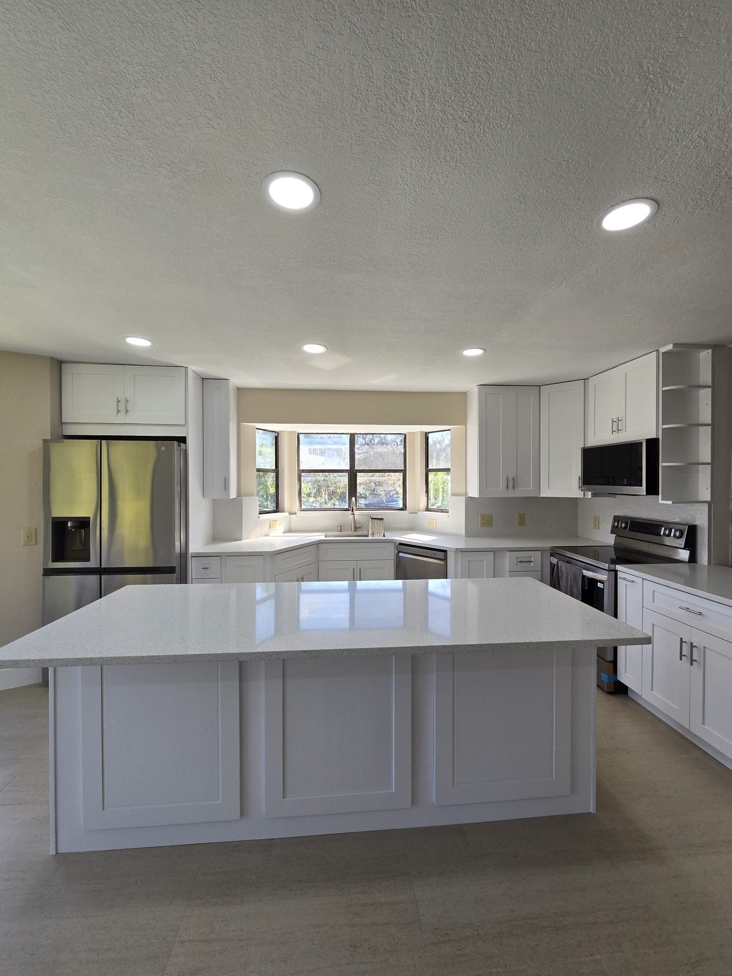 A bright kitchen featuring white cabinets, and a large central island with a white countertop, Service available in St. Cloud