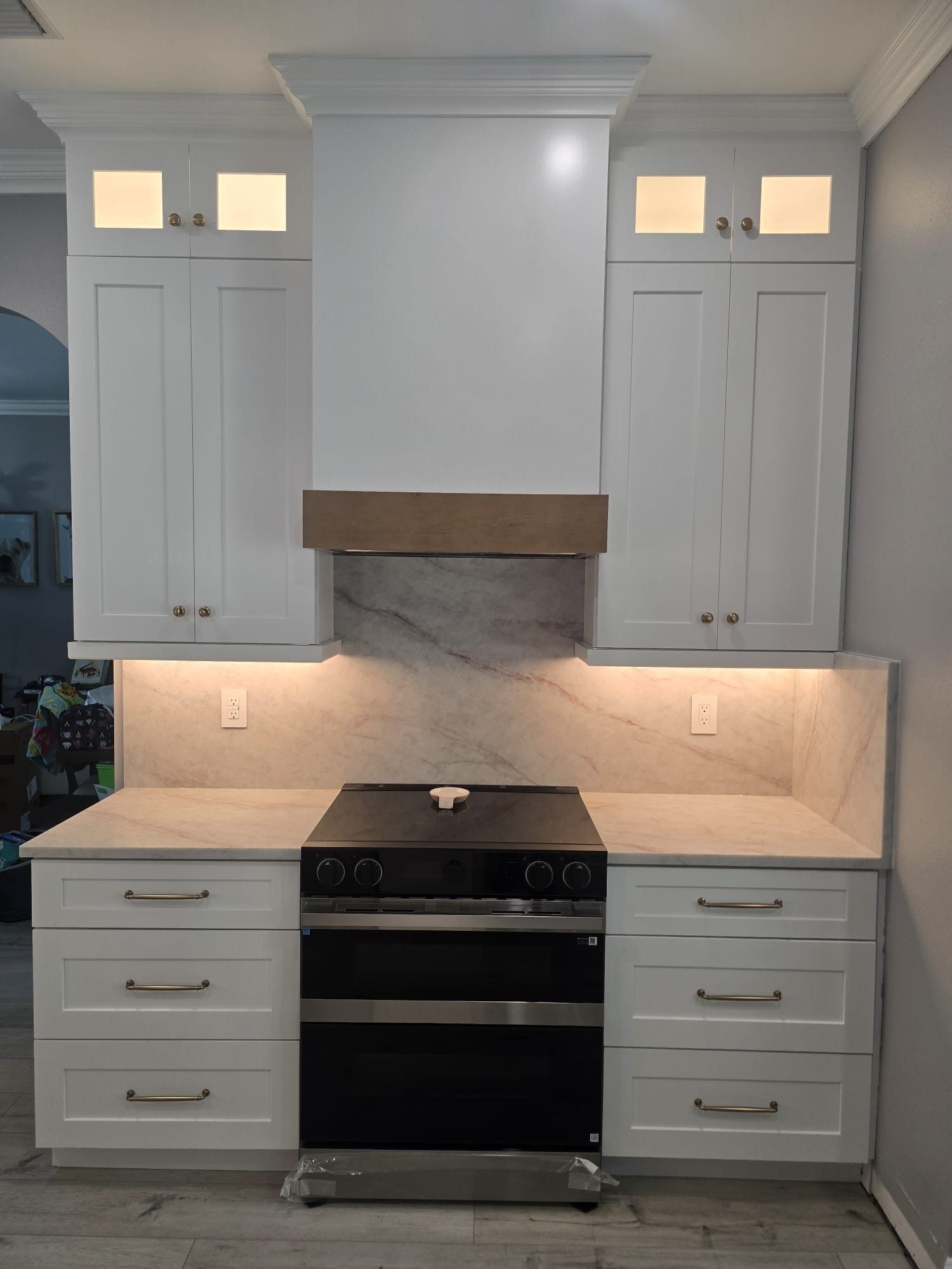 White kitchen cabinets and drawers flank a stainless steel stove with a wooden range hood. Serving Orlando